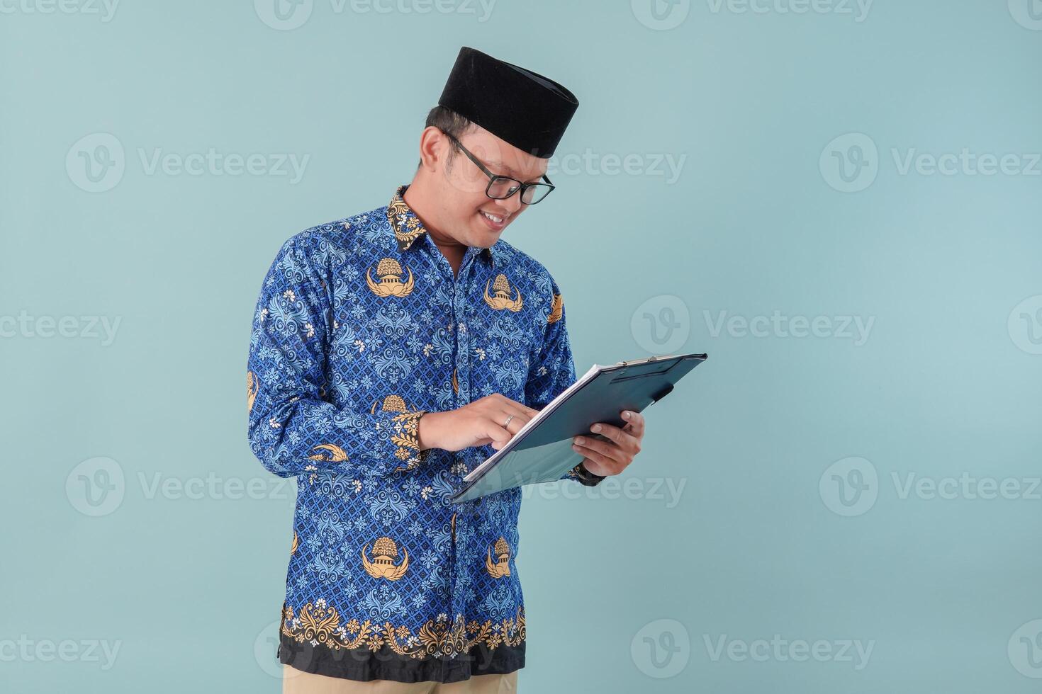 Handsome government worker man wearing blue batik uniform reading and checking document paper. photo