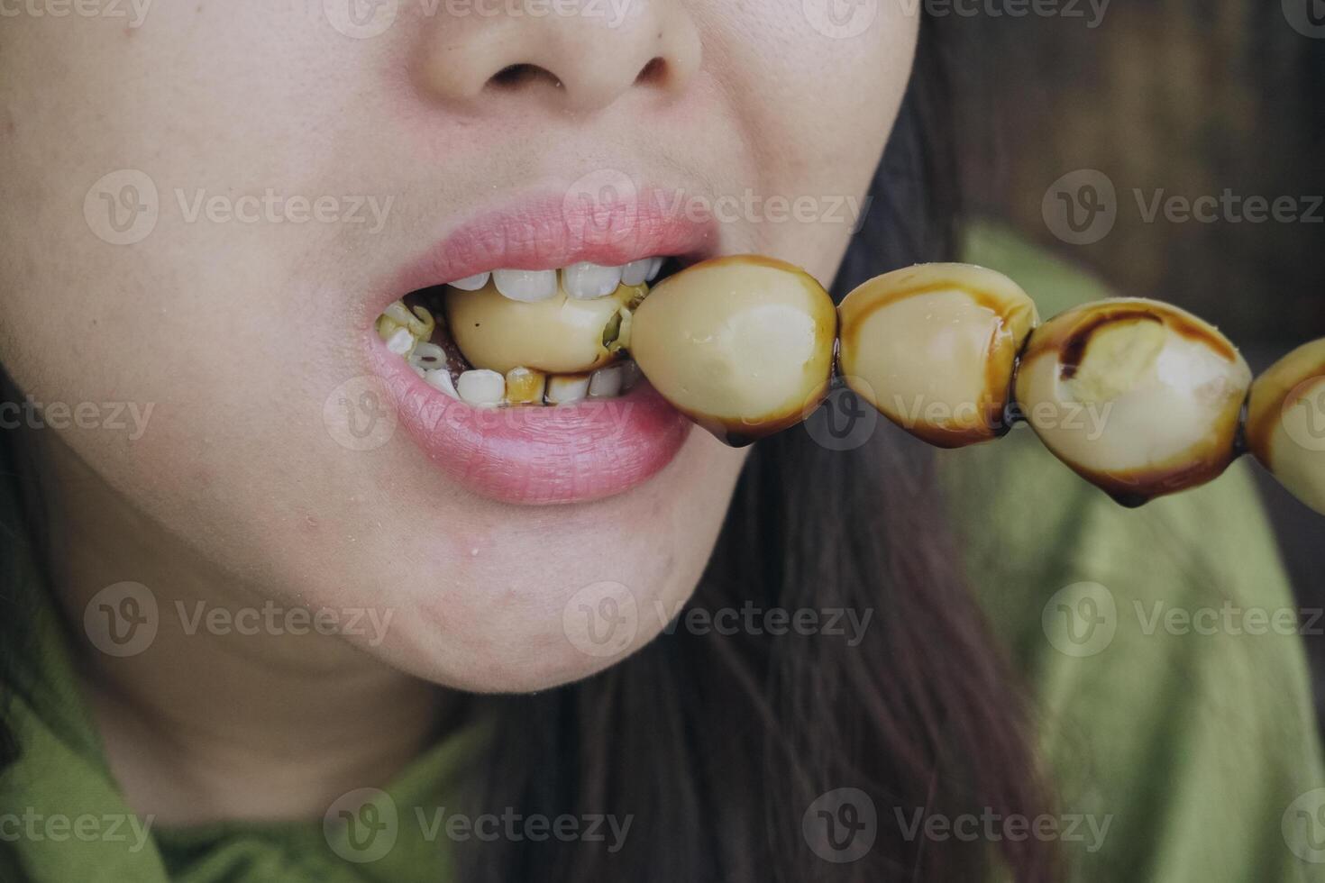 Close up portrait of Asian woman eating a skewer made from quail eggs poured by soy sauce on top. photo