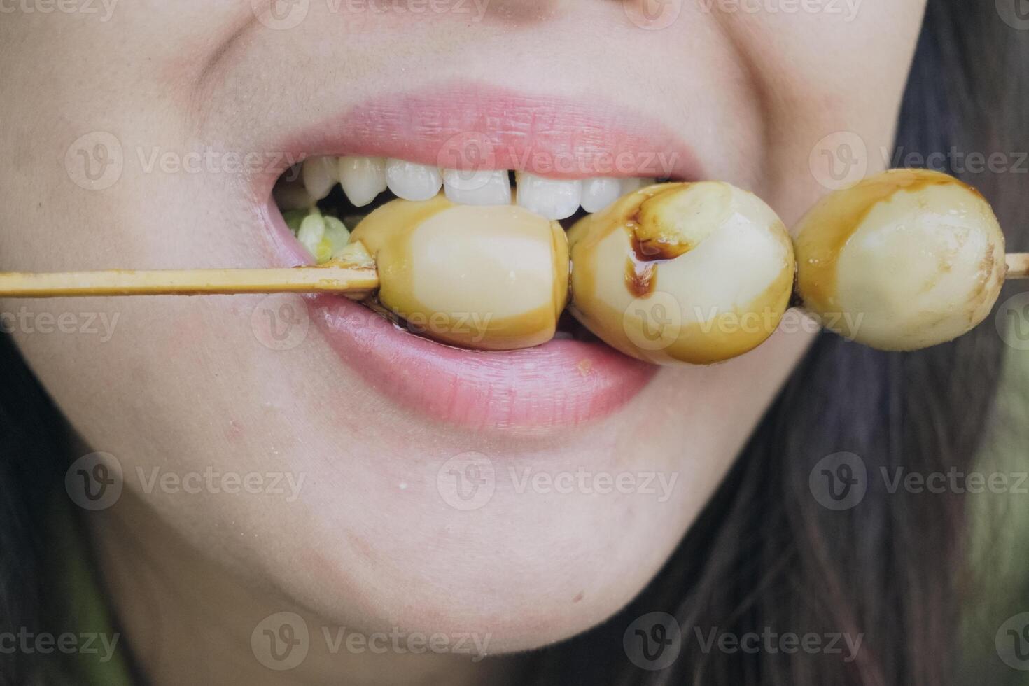 Close up portrait of Asian woman eating a skewer made from quail eggs poured by soy sauce on top. photo