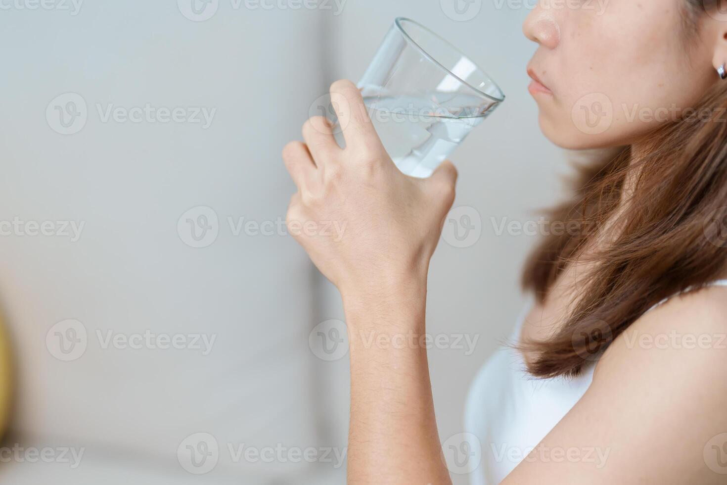 Happy woman holding water glass, female drinking pure water on sofa at home. Healthy, Refreshment, lifestyle and daily routine concept photo