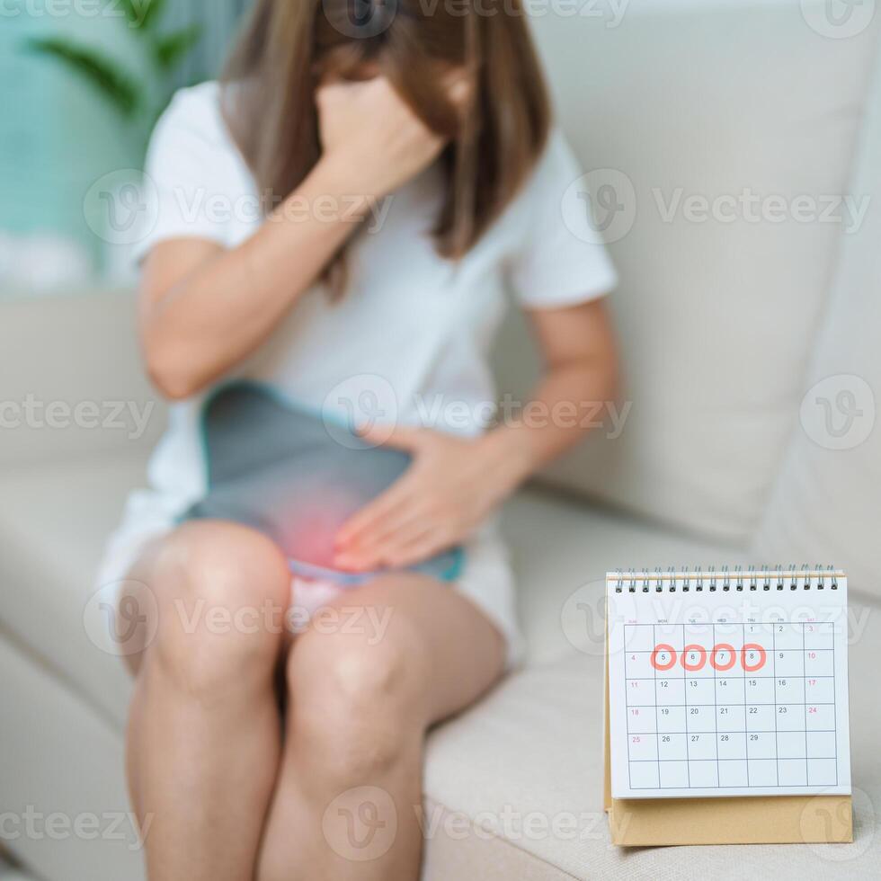 Menstruation period cycle of monthly and Stomachache concepts. woman having abdomen pain with hot water bottle and calendar, illness female suffer from premenstrual ache and body Health problem photo