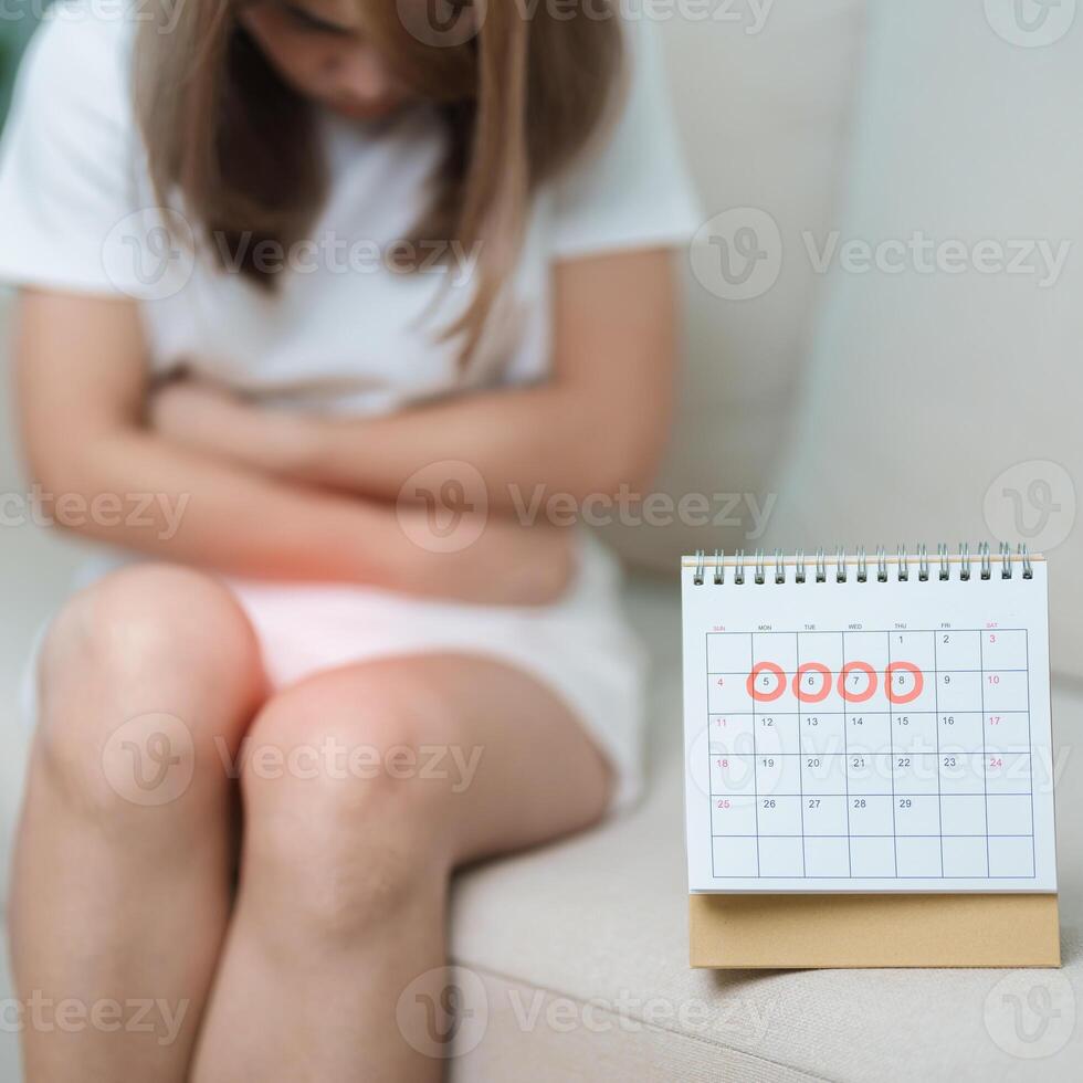 Menstruation period cycle of monthly and Stomachache concepts. woman having abdomen pain with calendar, illness female suffer from premenstrual ache and body Health problem on sofa at home photo