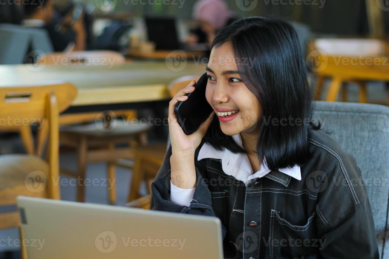 attractive and pretty asian woman make phone call with client and using laptop in cafe photo