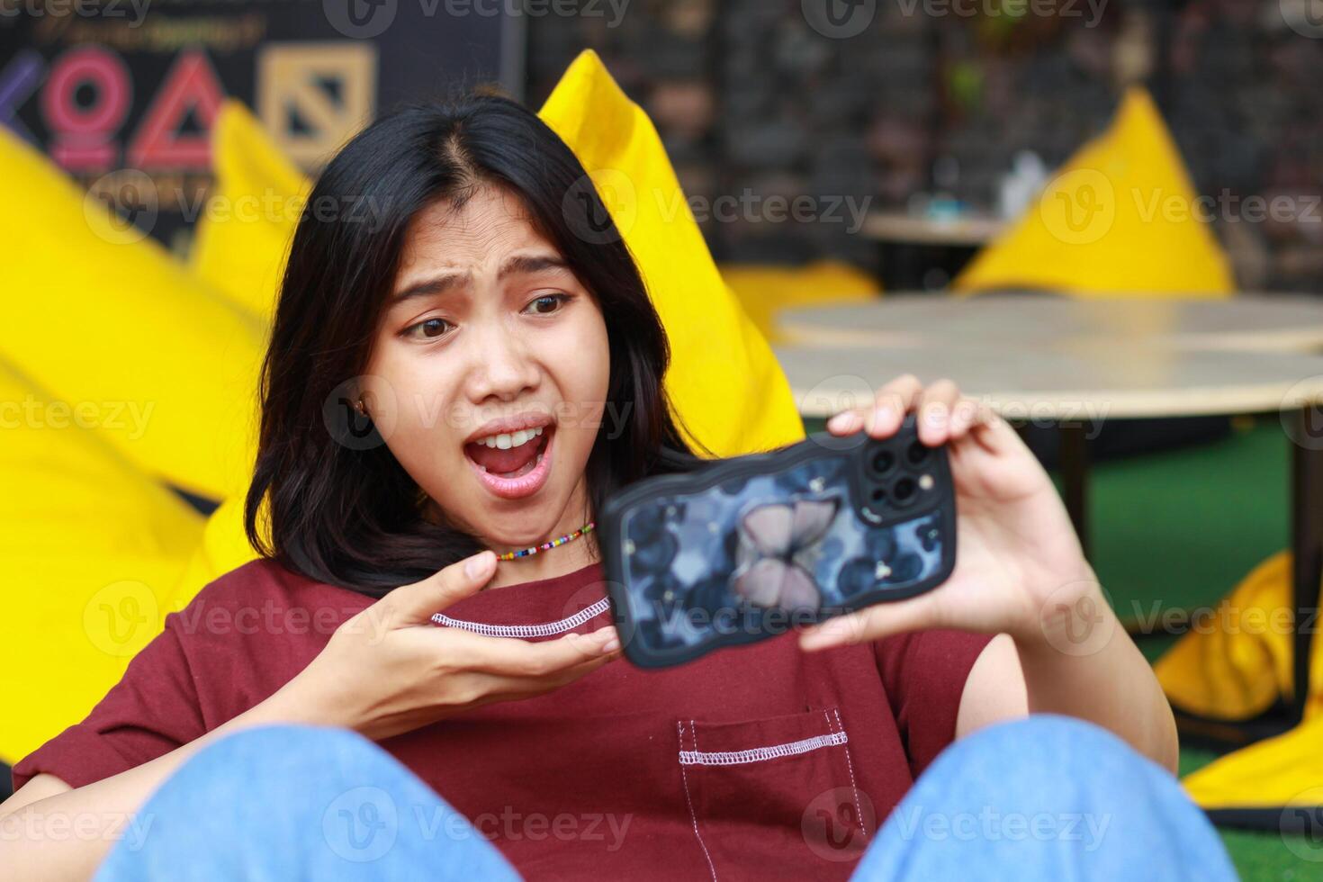 shocked asian woman defeated playing game using smartphone in outdoor cafe sitting in bean and covering her mouth photo