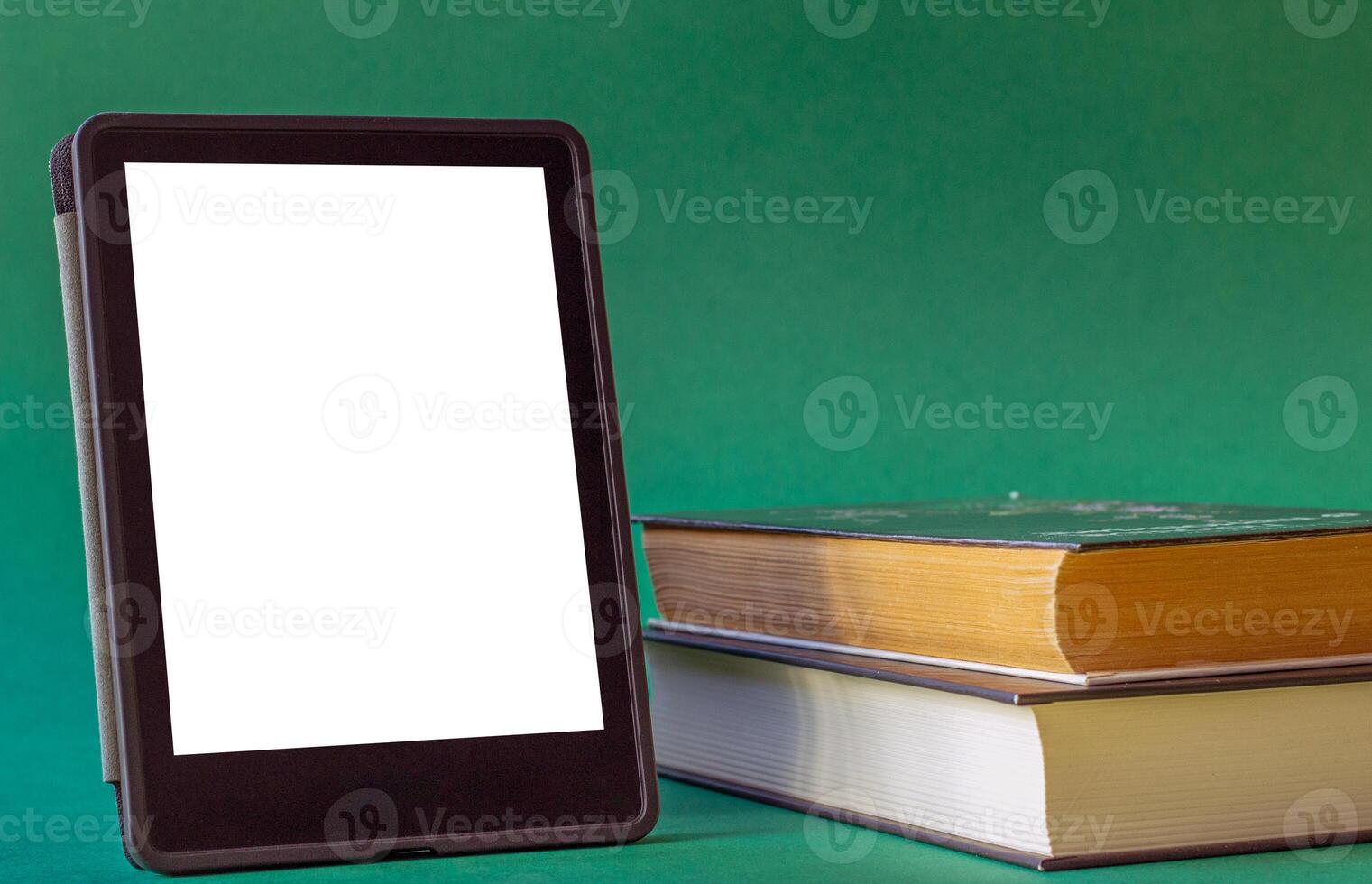 an electronic book next to a stack of paper books on a dark green background. one e-book replaces many regular books photo