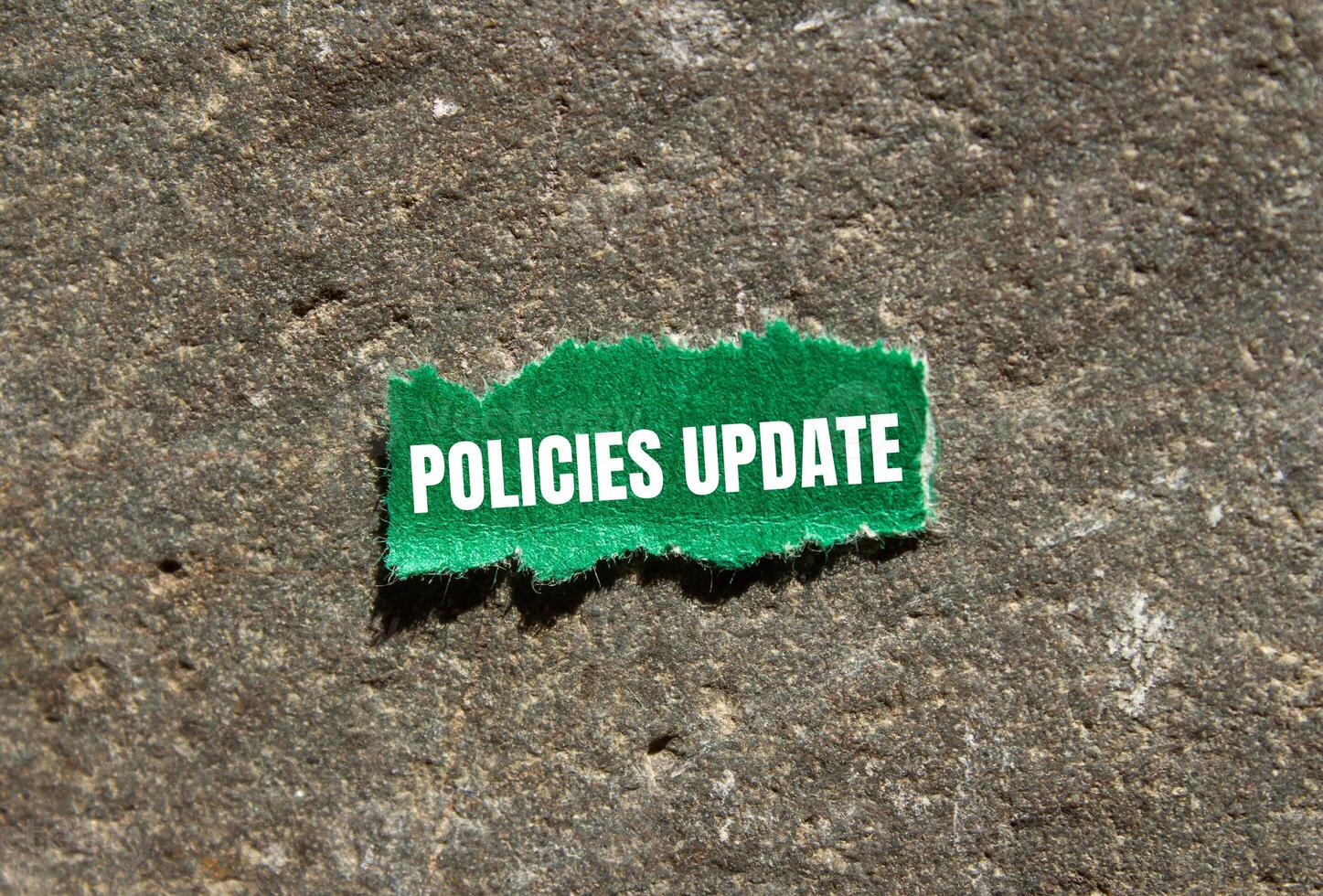 Policies update message written on ripped green torn paper piece with stone background. Conceptual policies update symbol. Copy space. photo