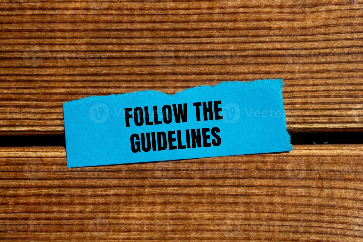 Follow the guidelines message written on ripped torn blue paper piece with wooden background. Conceptual follow the guidelines symbol. Copy space. photo