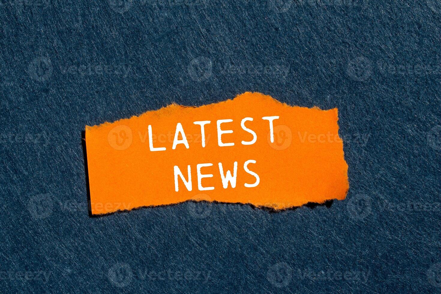 Latest news message written on ripped torn orange paper piece with gray felt background. Conceptual latest news symbol. Copy space. photo