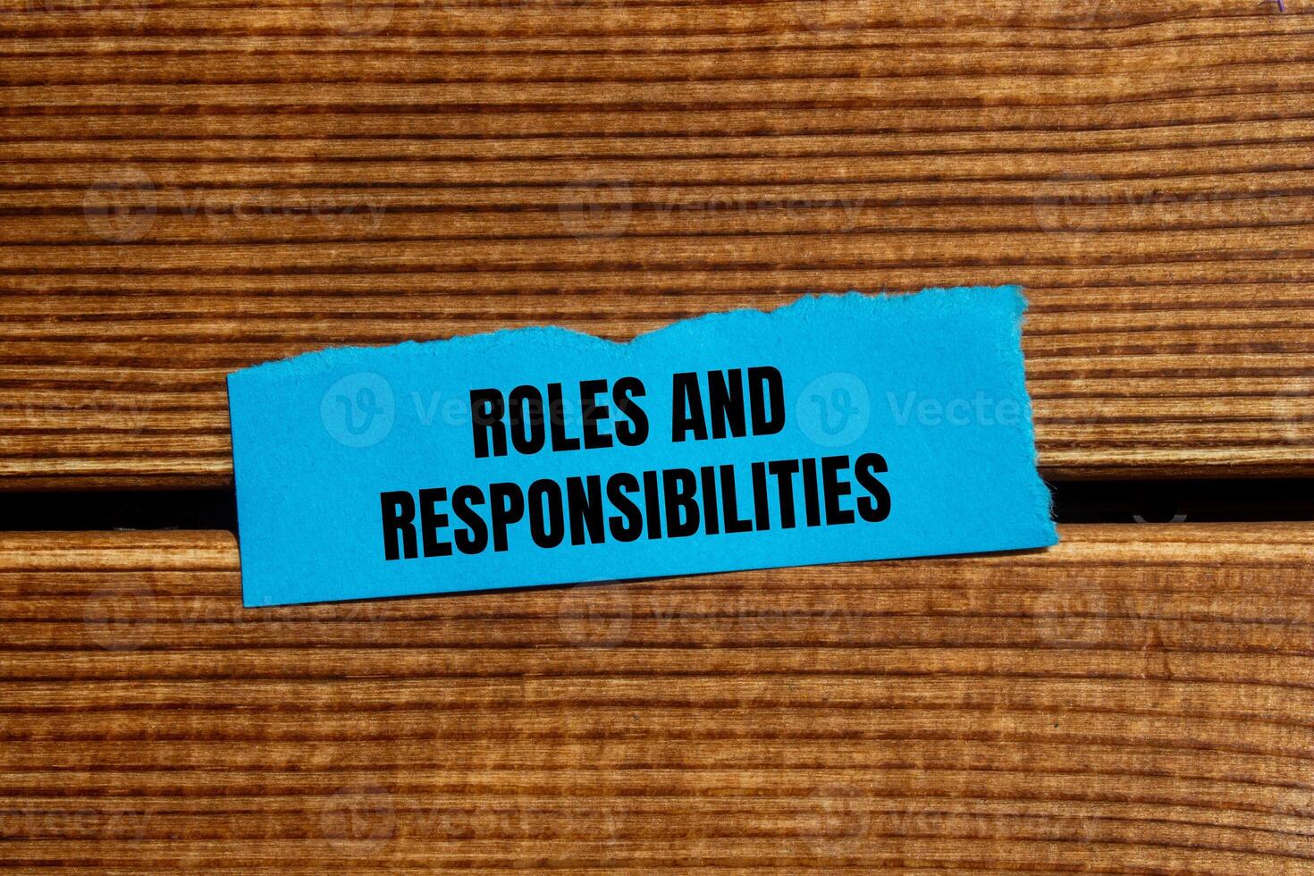 Roles and responsibilities message written on ripped torn blue paper piece with wooden background. Conceptual roles and responsibilities symbol. Copy space. photo
