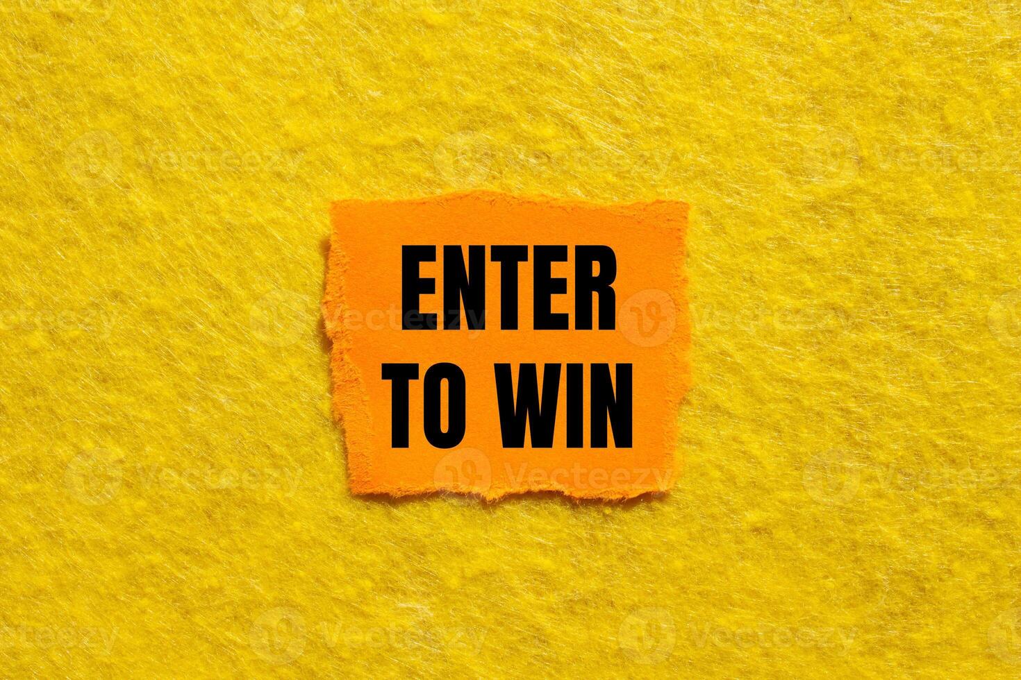 Enter to win message written on ripped torn orange paper piece with yellow background. Conceptual enter to win symbol. Copy space. photo