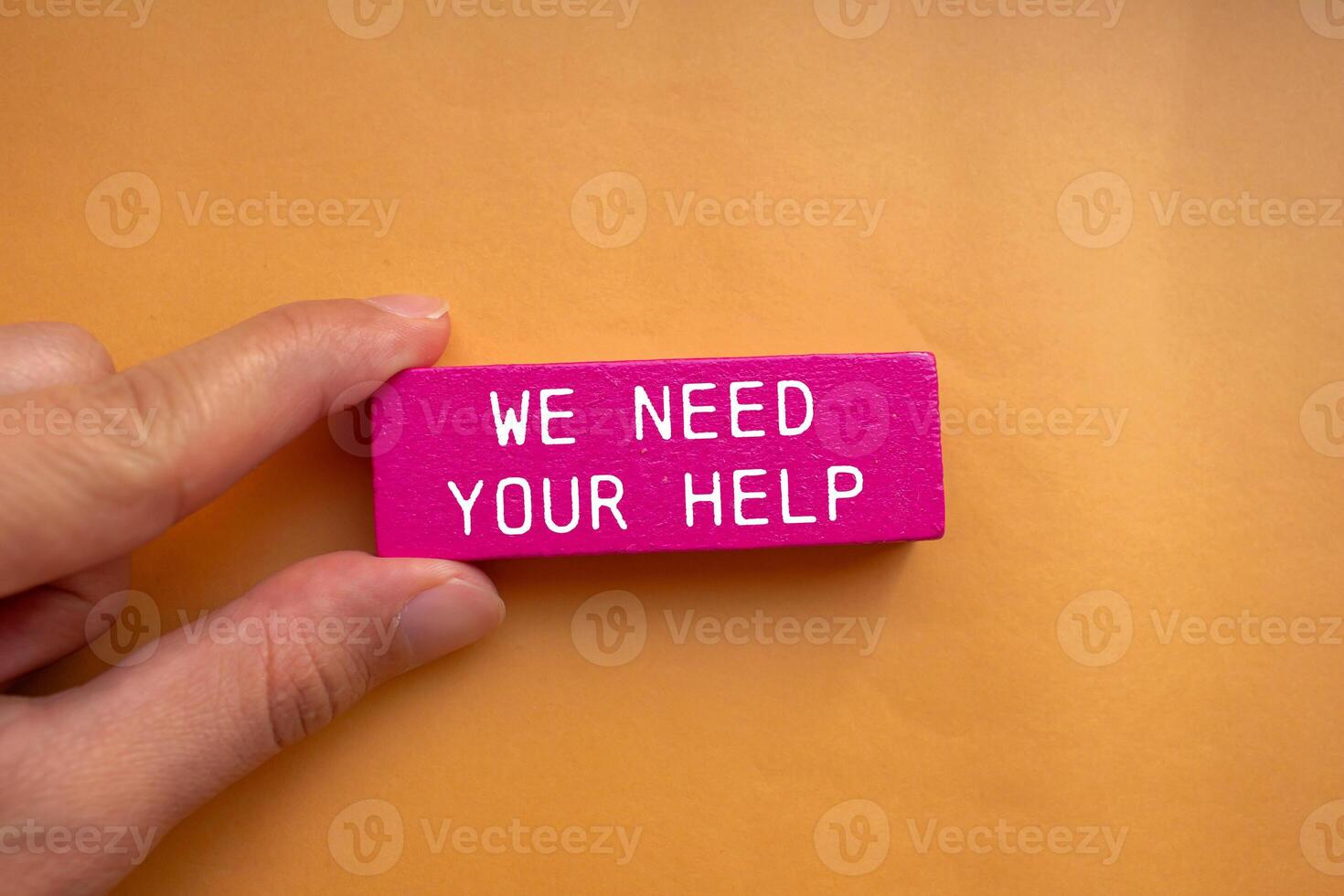 We need your help message written on pink wooden block with orange background. Conceptual we need your help symbol. Copy space. photo