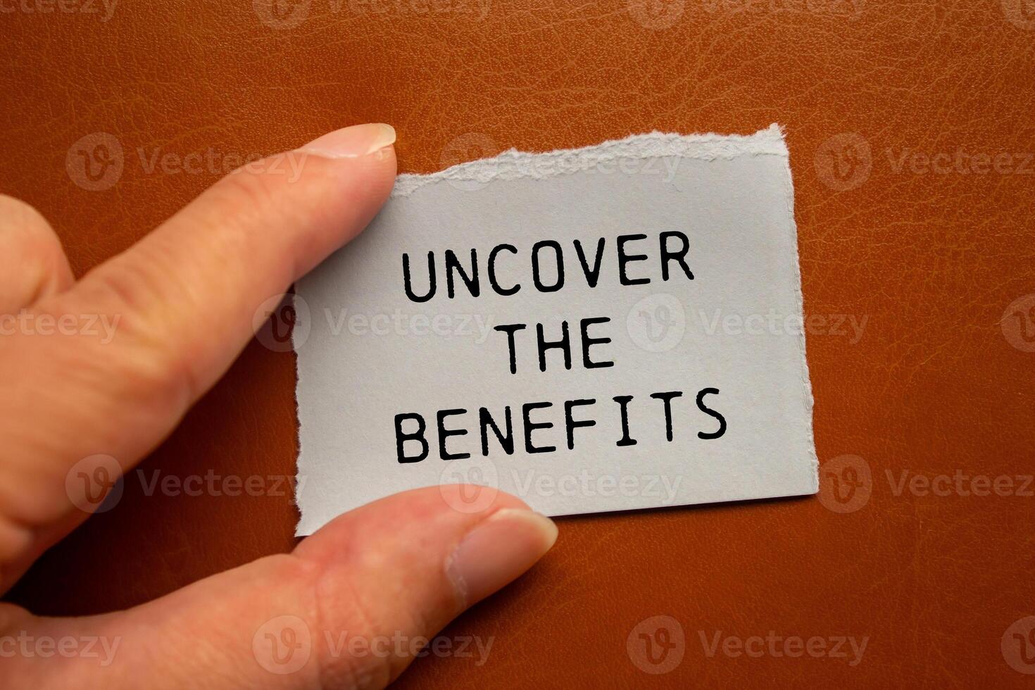 Uncover the benefits message written on ripped torn paper piece on brown background. Conceptual uncover the benefits symbol. Copy space. photo