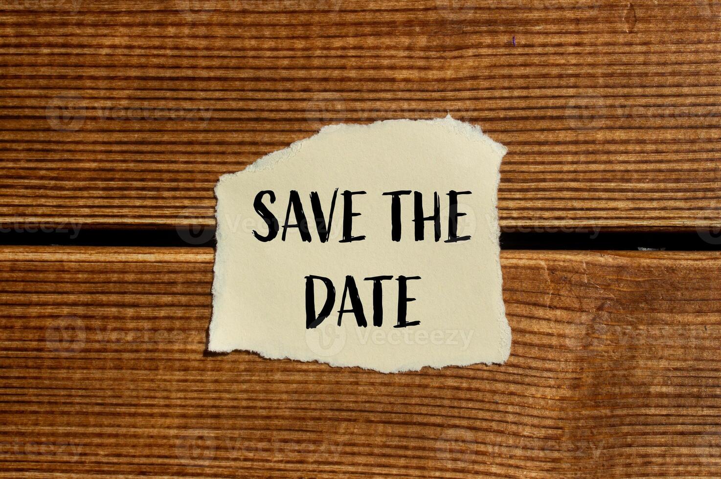 Save the date message written on ripped torn paper with wooden background. Conceptual save the date symbol. Copy space. photo