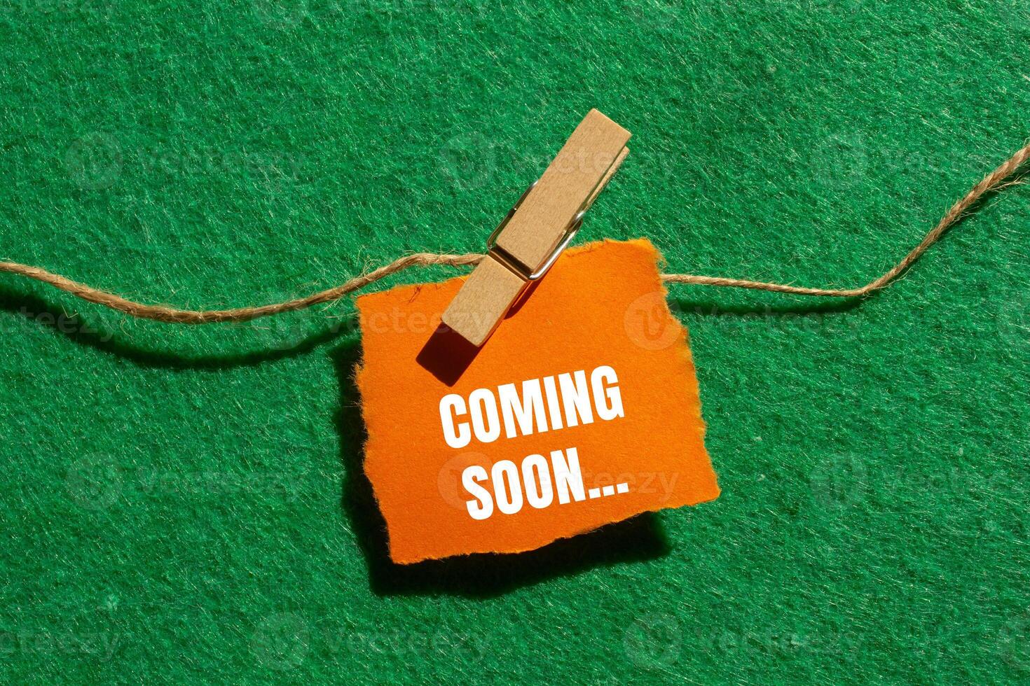 Coming soon message written on ripped torn orange paper piece with green background. Conceptual coming soon symbol. Copy space. photo