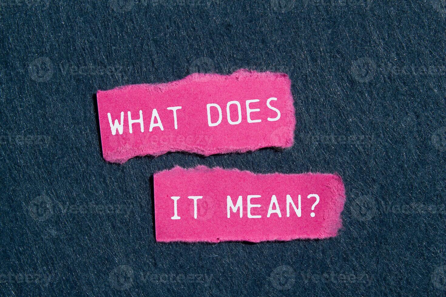 What does it mean question written on ripped torn pink paper pieces on gray background. Conceptual what does it mean question symbol. Copy space. photo