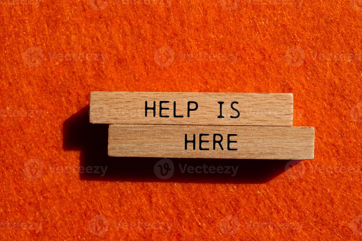 Help is here message written on wooden blocks on orange felt background. Conceptual help is here symbol. Copy space. photo