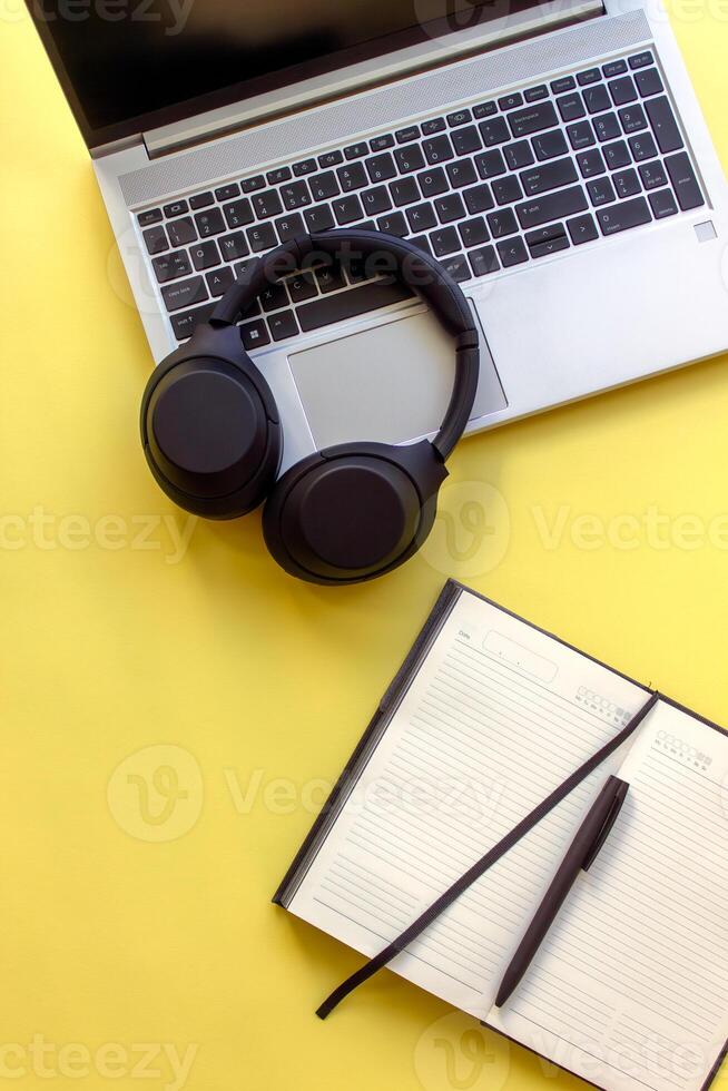 vertical image, mobile web banner. laptop, notebook with pen and wireless headphones on a bright yellow background. student study kit.Perfect for themes related to education, art, and office aesthetic photo
