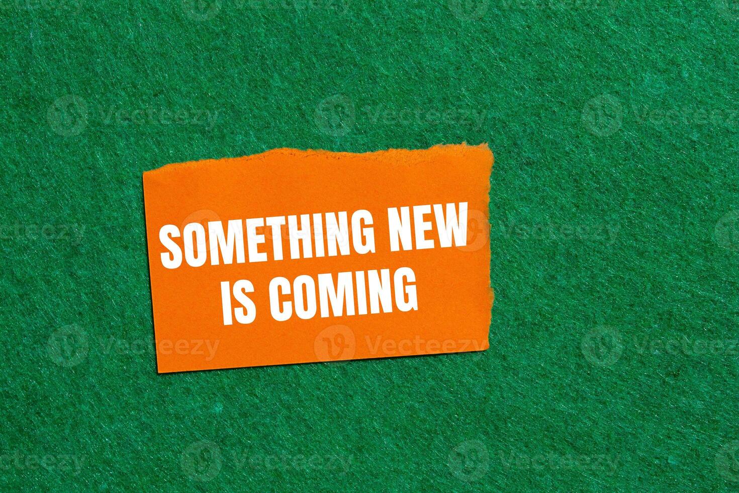 Something new is coming message written on ripped orange torn paper piece on green background. Conceptual something new is coming symbol. Copy space. photo