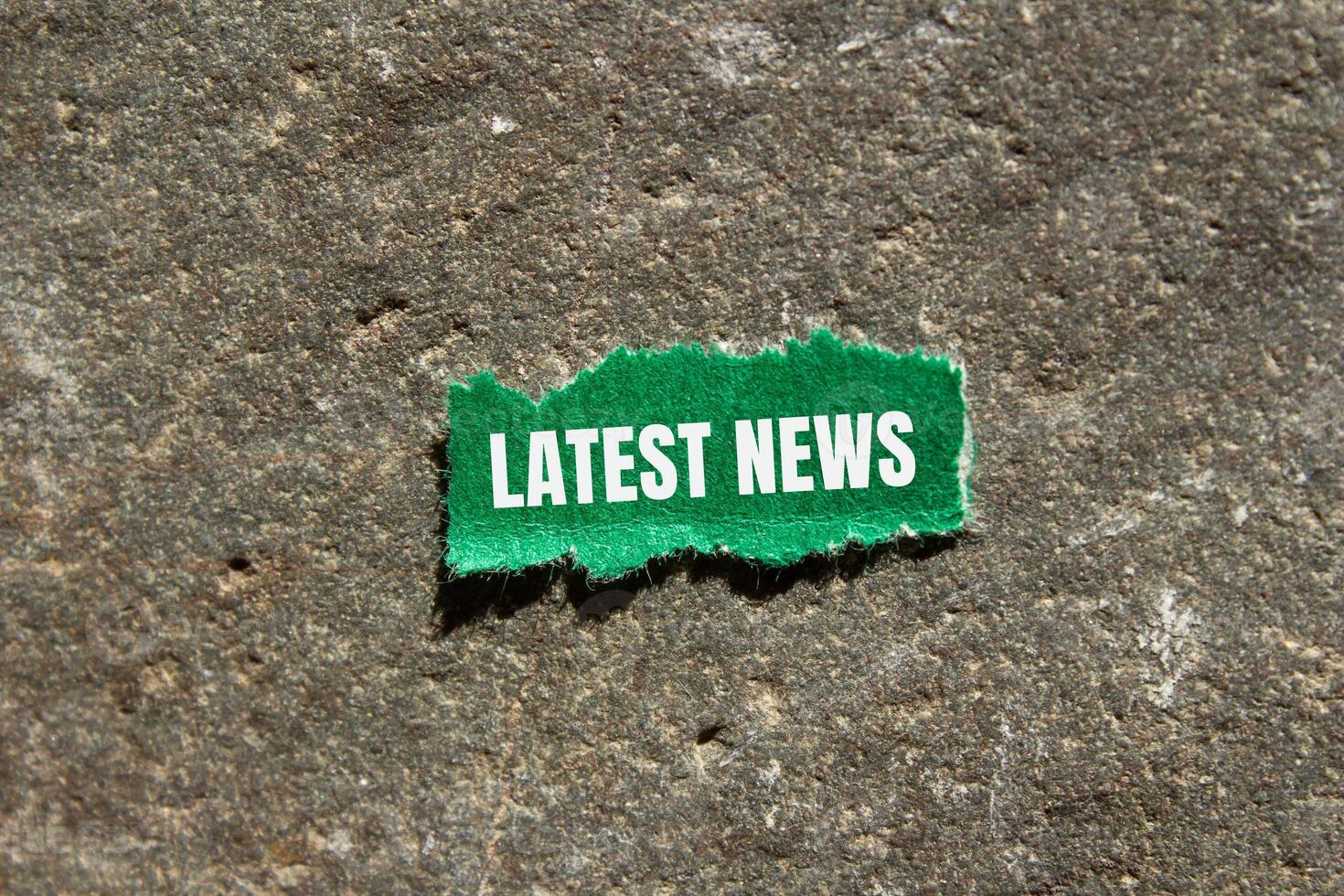Latest news message written on ripped green torn paper piece with stone background. Conceptual latest news symbol. Copy space. photo