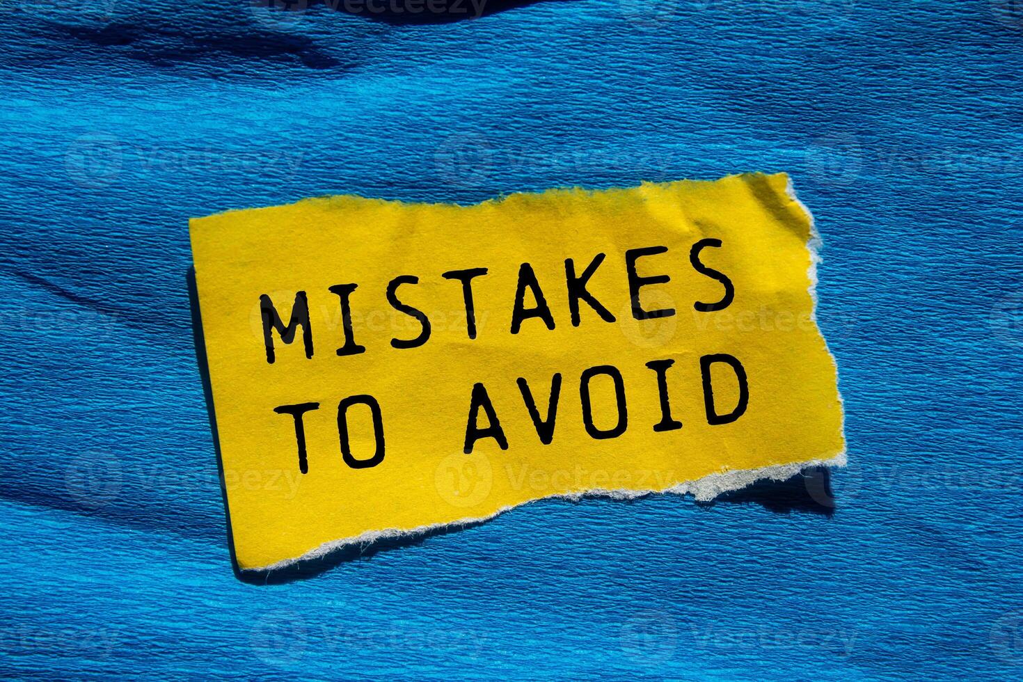 Mistakes to avoid message written on ripped torn yellow paper piece with blue background. Conceptual mistakes to avoid symbol. Copy space. photo