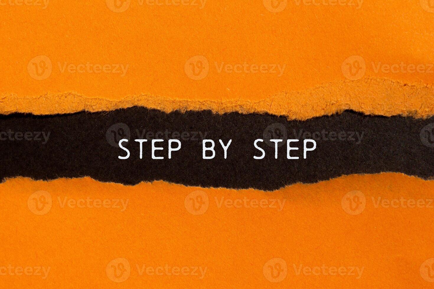 Step by step message written on ripped torn orange paper on black background. Conceptual step by step symbol. Copy space. photo