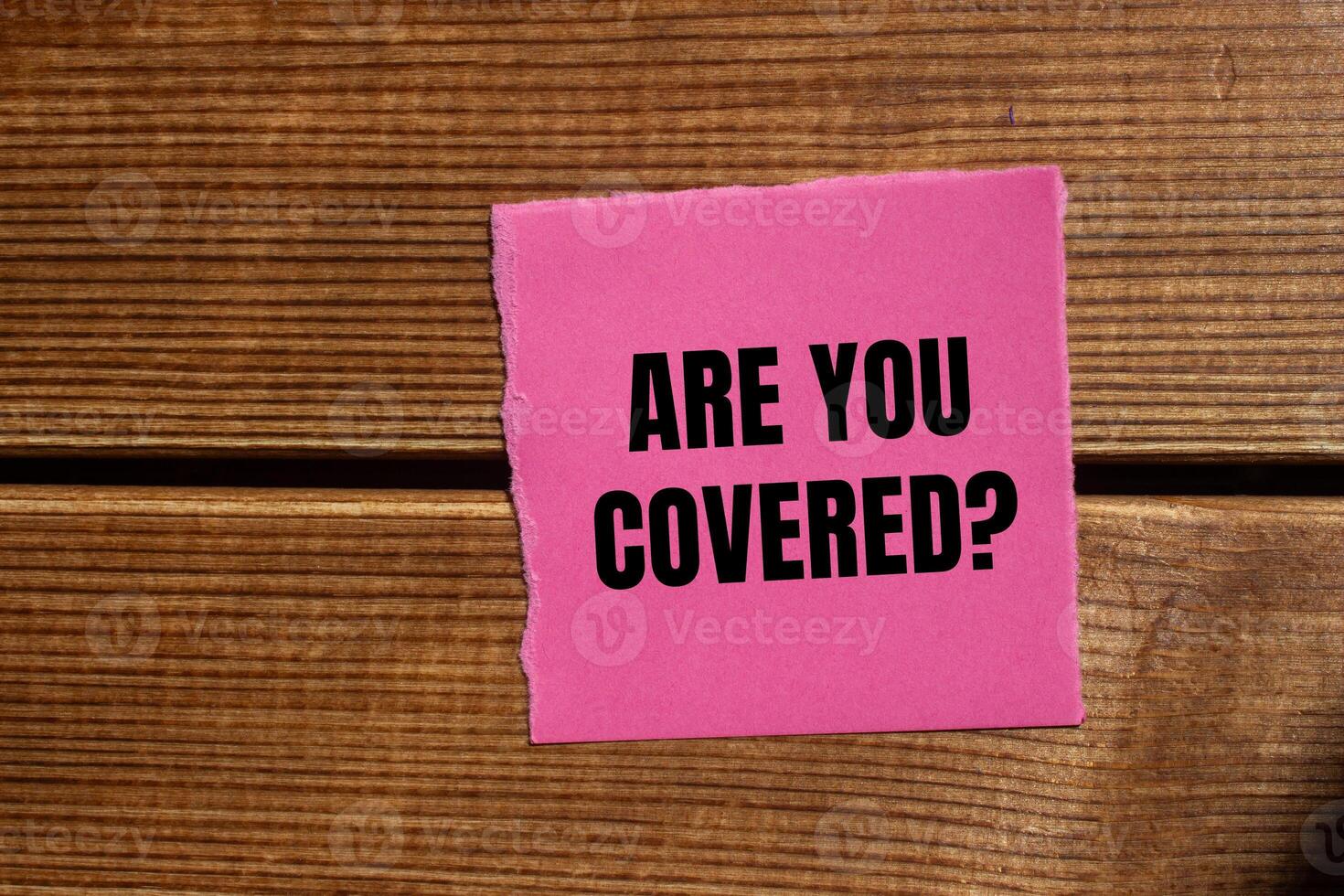 Are you covered question written on ripped torn pink paper piece with wooden background. Conceptual are you covered question symbol. Copy space. photo