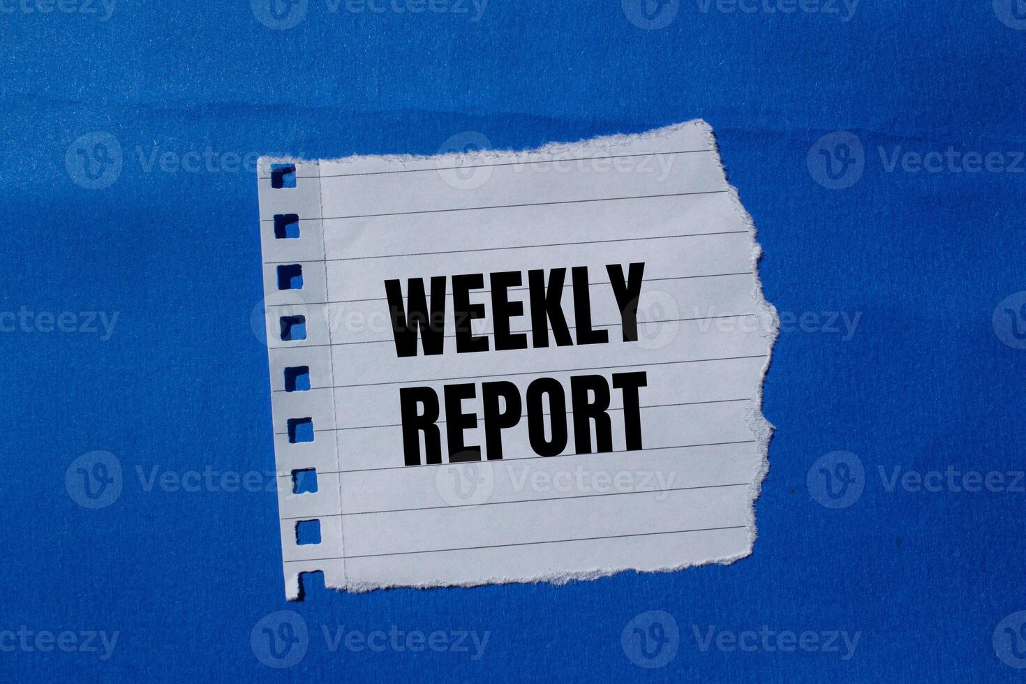 Weekly report message written on ripped torn paper piece with blue background. Conceptual weekly report symbol. Copy space. photo