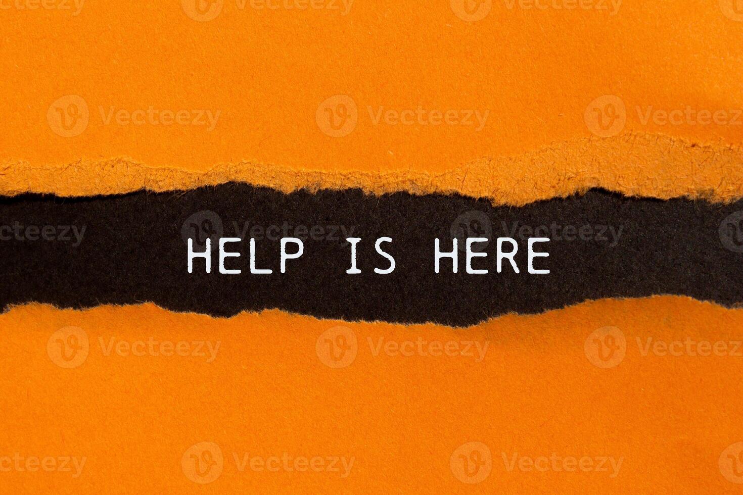 Help is here message written on ripped torn orange paper on black background. Conceptual help is here symbol. Copy space. photo