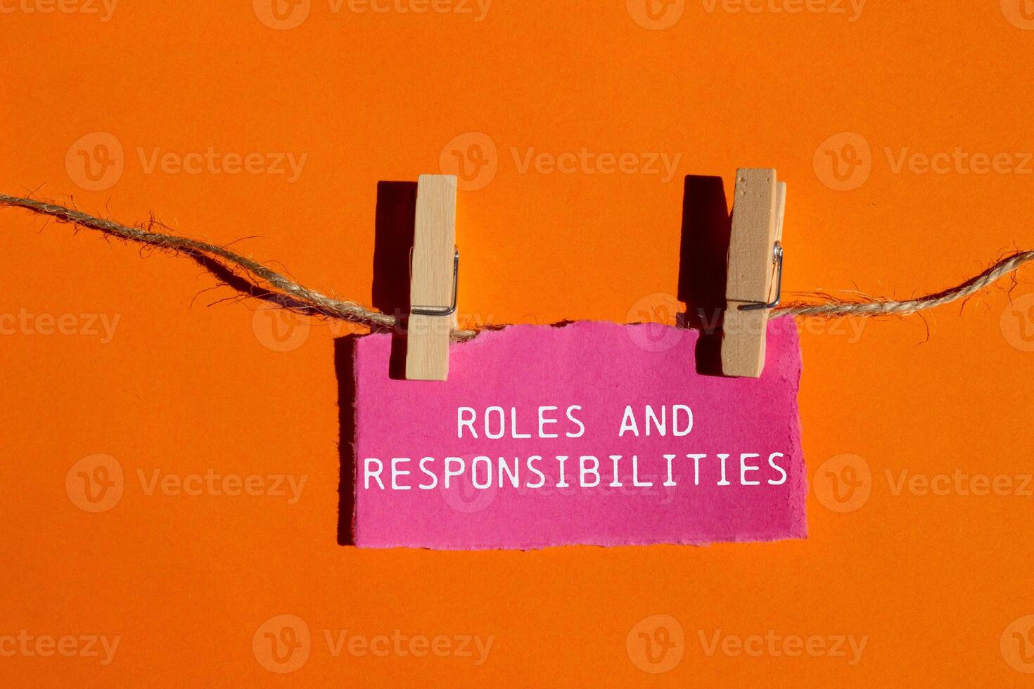 Roles and responsibilities message written on ripped pink torn paper piece on orange background. Conceptual roles and responsibilities symbol. Copy space. photo