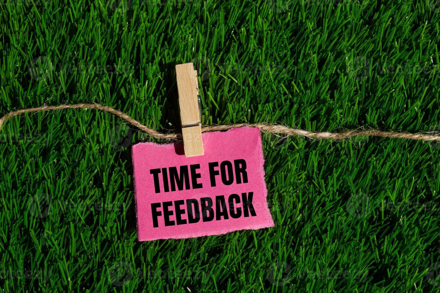 Time for feedback message written on ripped torn pink paper piece with green grass background. Conceptual time for feedback symbol. Copy space. photo