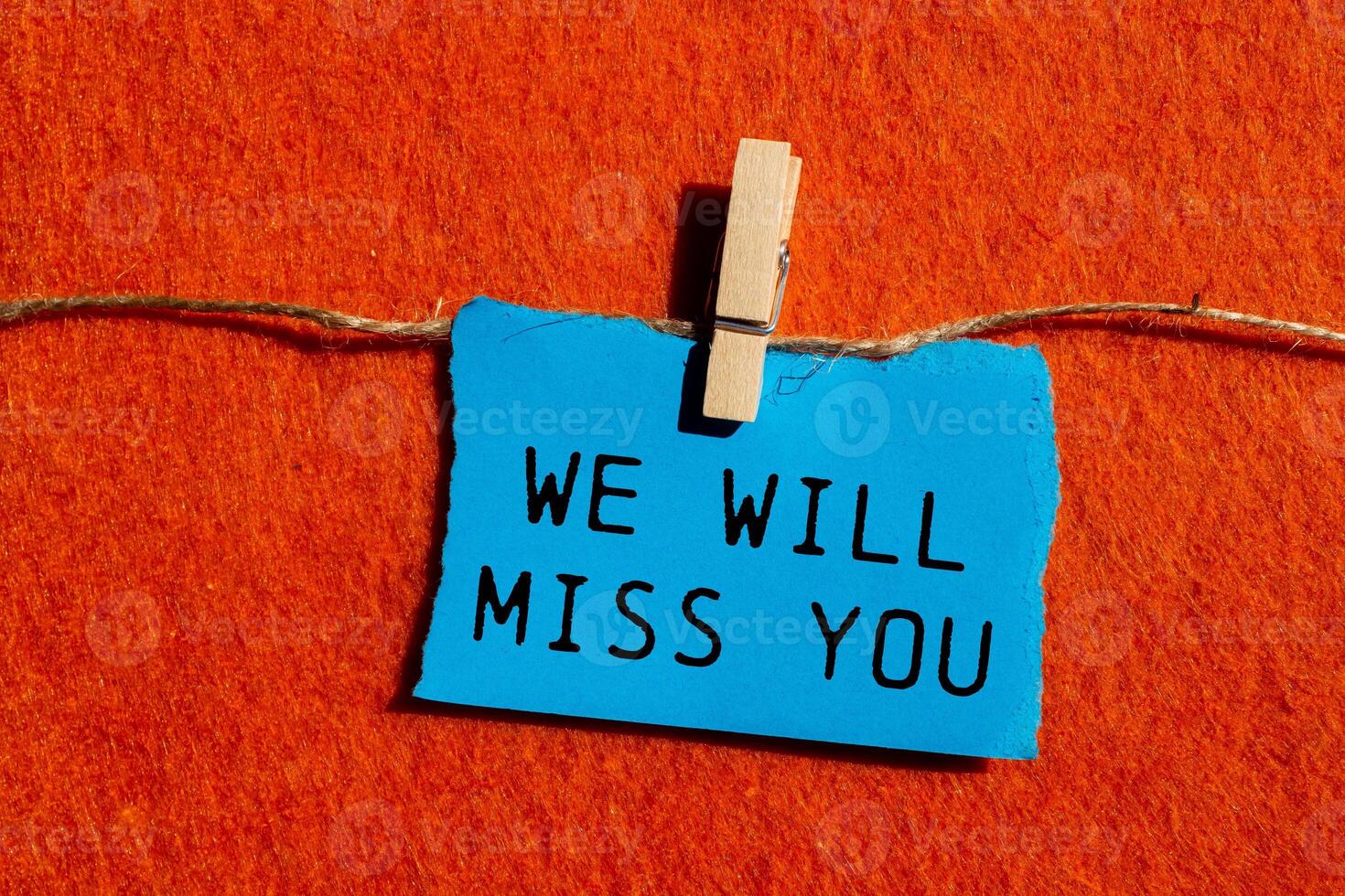 We will miss you message written on ripped blue torn paper piece on orange background. Conceptual we will miss you symbol. Copy space. photo