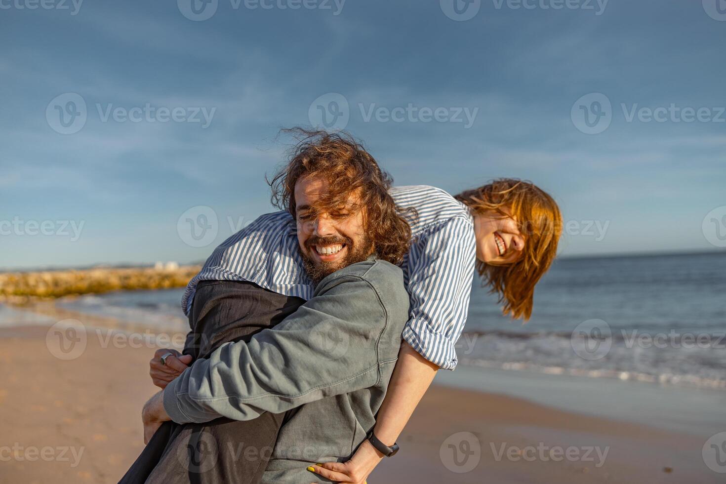 Smilng couple in love fool around while walking along the beach on sunny windy day photo