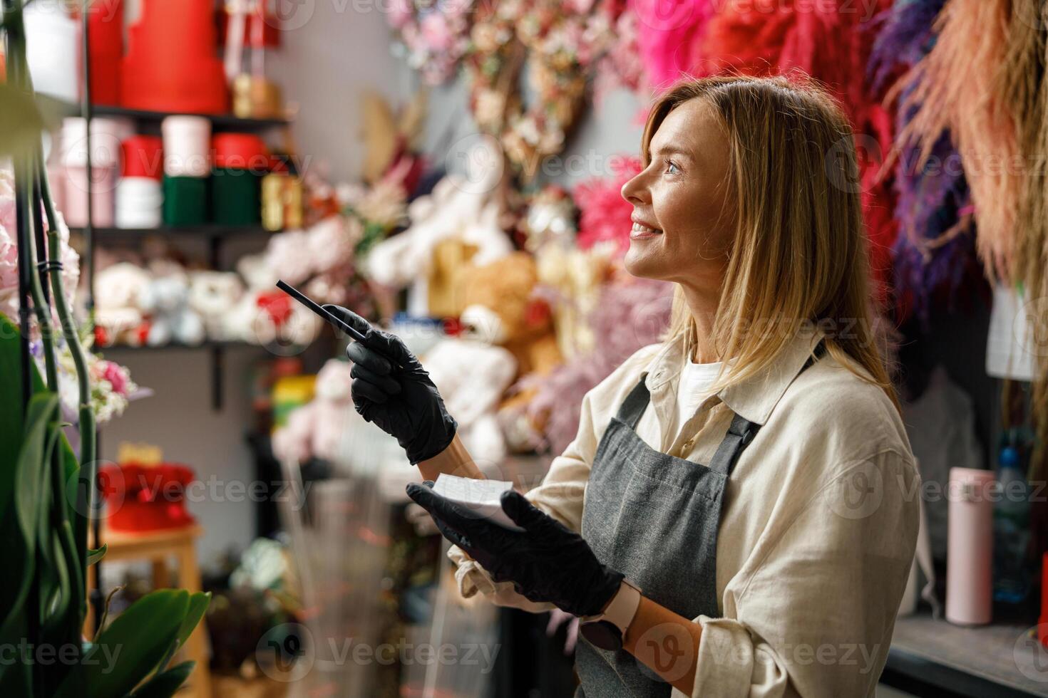 Smiling woman florist writing orders and customer information in notebook at flower shop photo