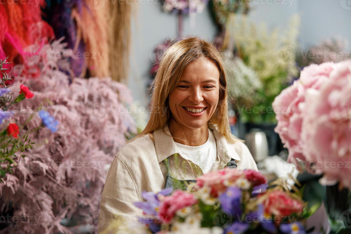 Smiling woman flower shop owner in apron looking on bouquet of flowers at florist store photo