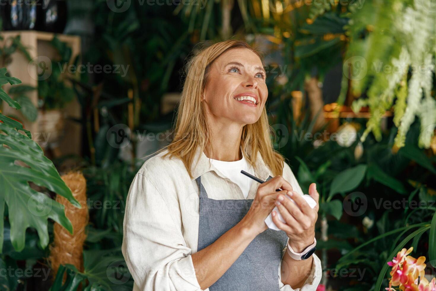 Smiling woman florist writing orders and customer information in notebook at flower shop photo