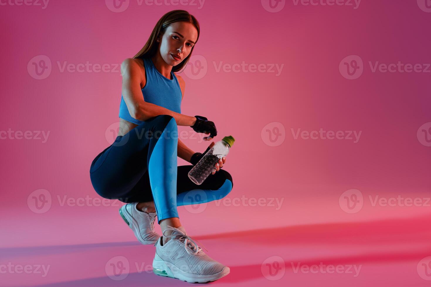 Healthy woman sitting with water bottle in sport clothing over studio background photo