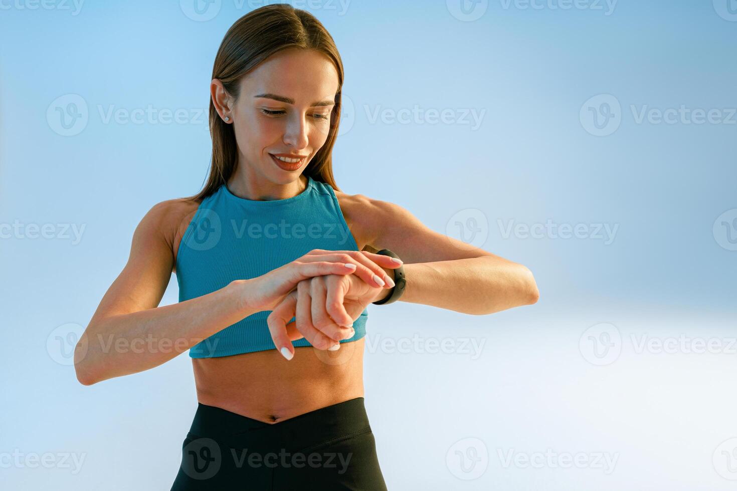 Smiling sporty woman standing and looking at watch checking her performance on studio background photo