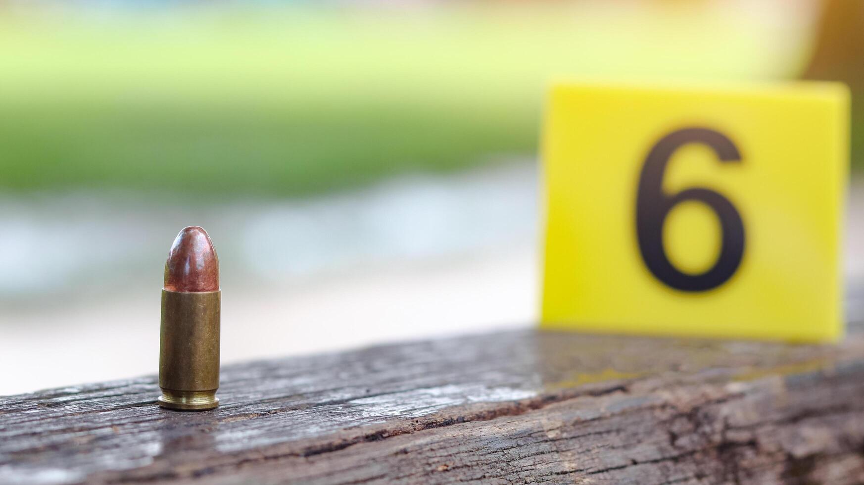 9 mm pistol bullet lying on dark wooden bench with blur number 6 sign on blur background. Concepts of criminal investigations and shooting sport. photo