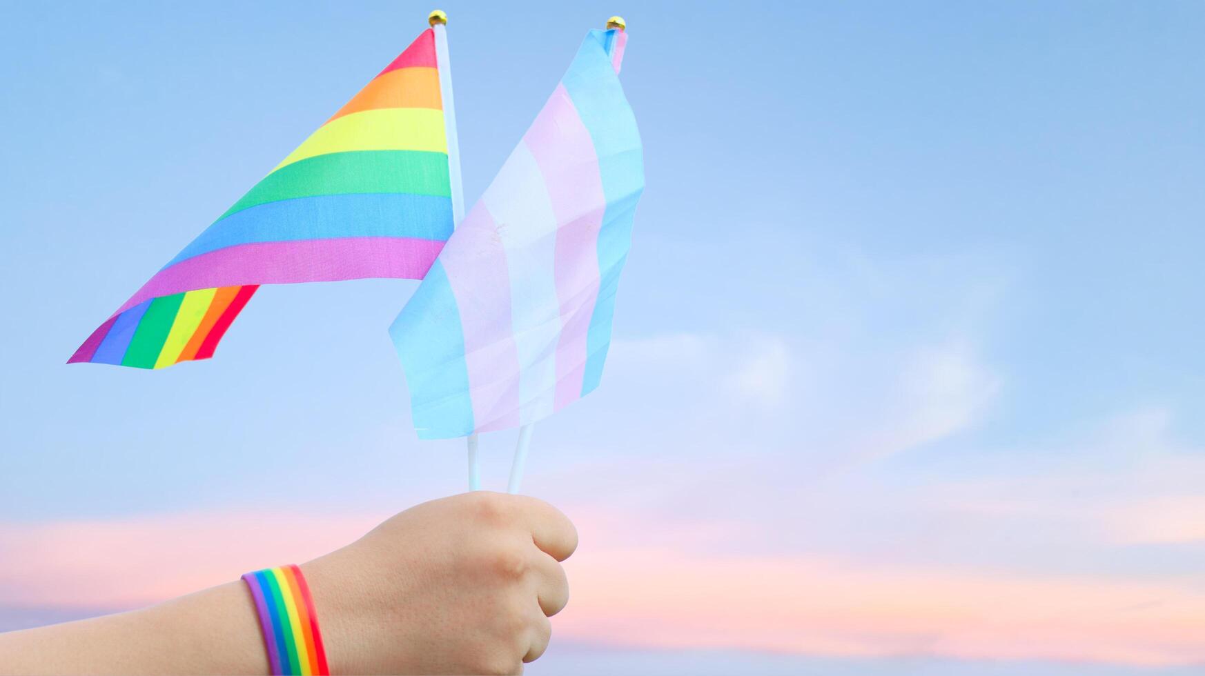 Cut out of hand holding both the LGBT flag and the LGBTQIA flag, set against blue sky background with clipping paths. The symbolizing unity, diversity, and inclusion. photo