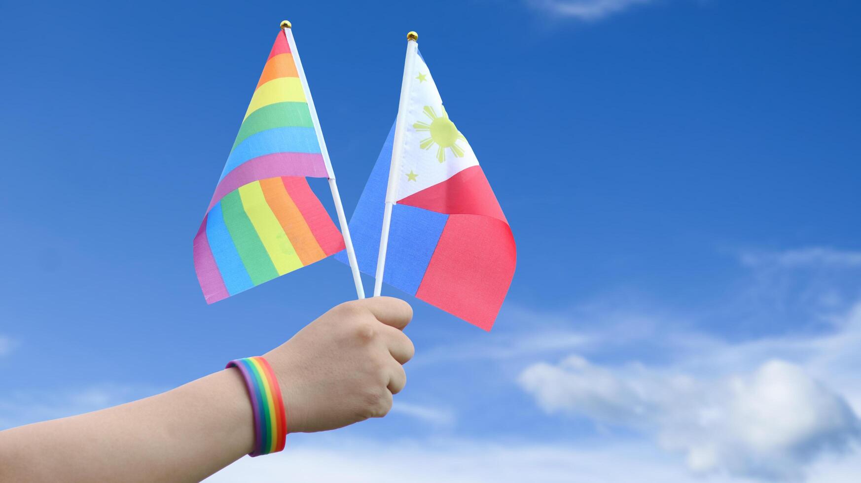 Cut out of hand holding both the LGBT flag and the Philippines flag, set against blue sky background with clipping paths. The symbolizing unity, diversity, and inclusion. photo