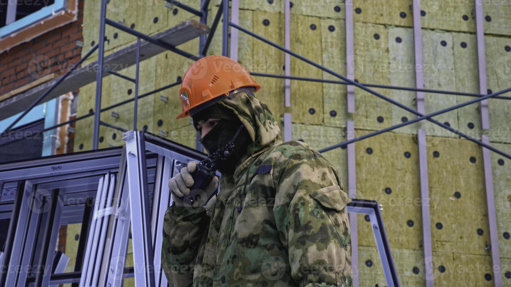 Man in work uniform speaks into walkie-talkie at construction site. Clip. Worker in helmet with walkie-talkie at construction site. Worker speaks into walkie-talkie at construction site photo