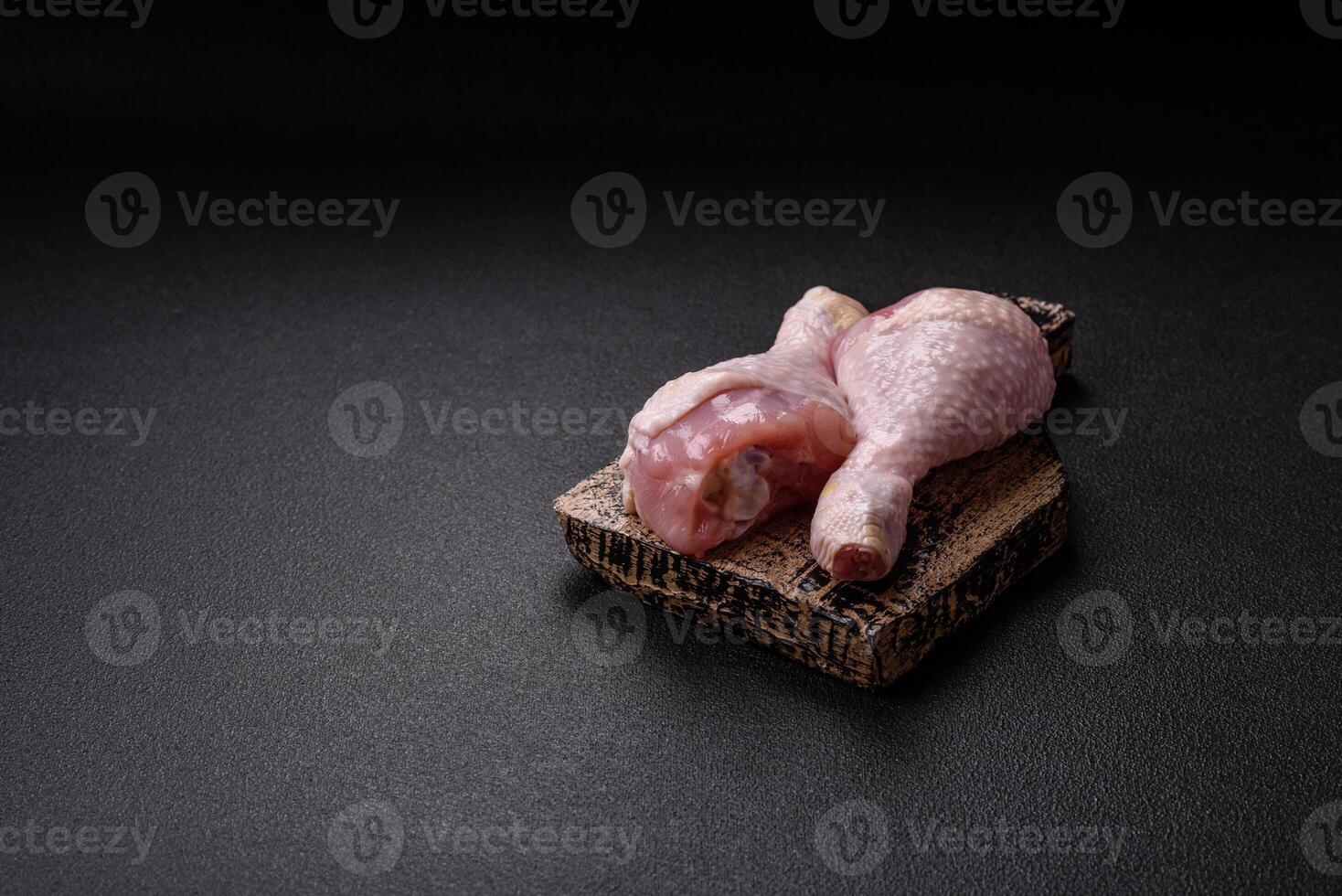 Raw chicken legs with salt, spices and herbs on a dark concrete background photo