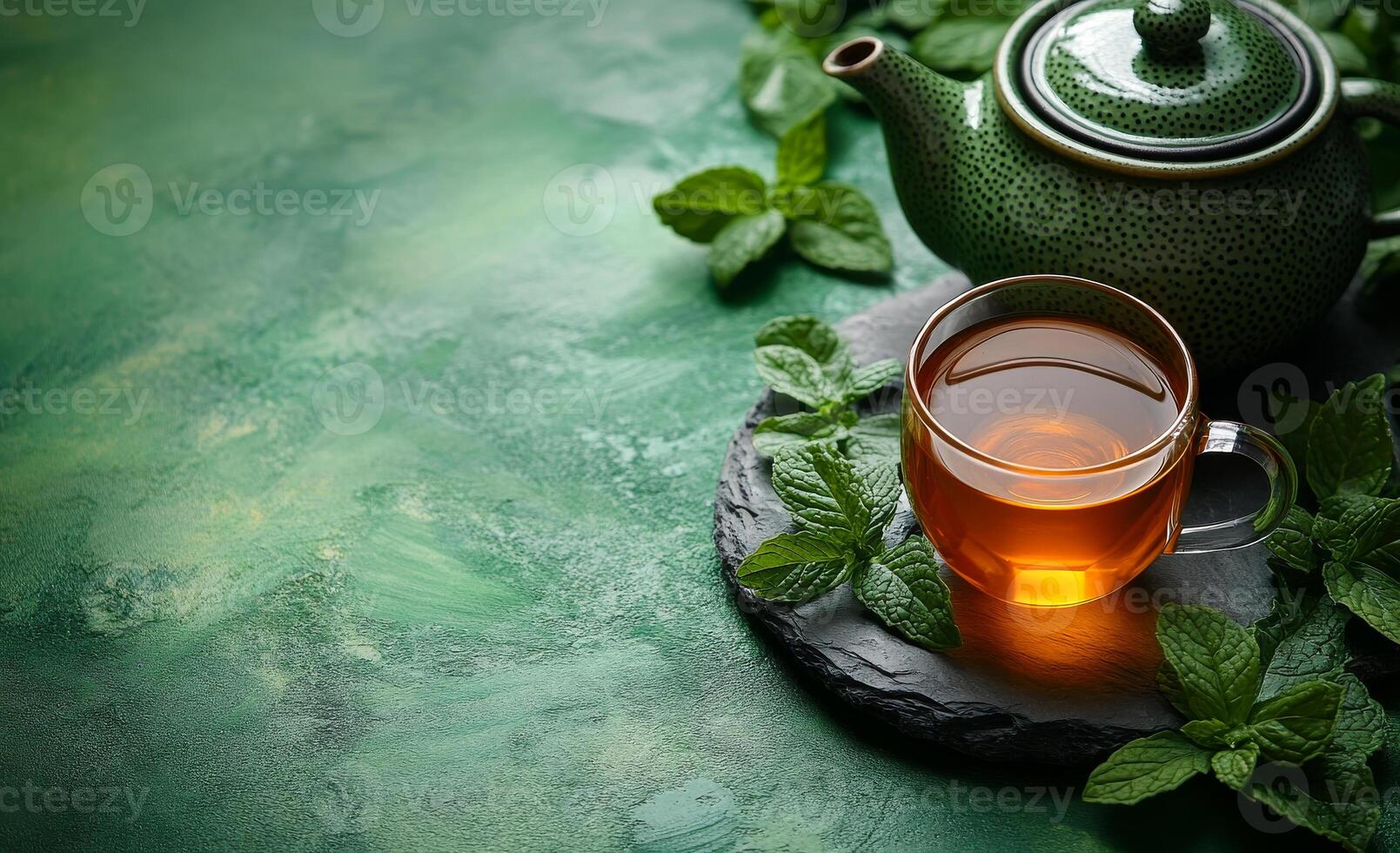 Refreshing mint tea served with a green teapot. A refreshing cup of mint tea rests on a stone coaster, surrounded by fresh mint leaves and a decorative green teapot. photo