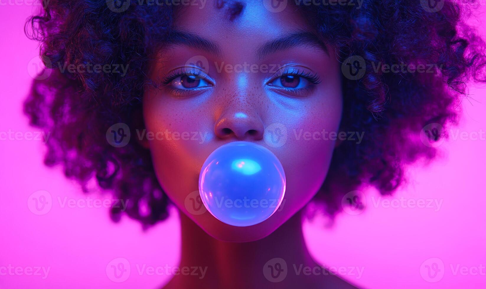 A woman with curly hair is blowing bubbles. The bubbles are blue and the woman is looking at the camera. The image has a fun and playful mood photo