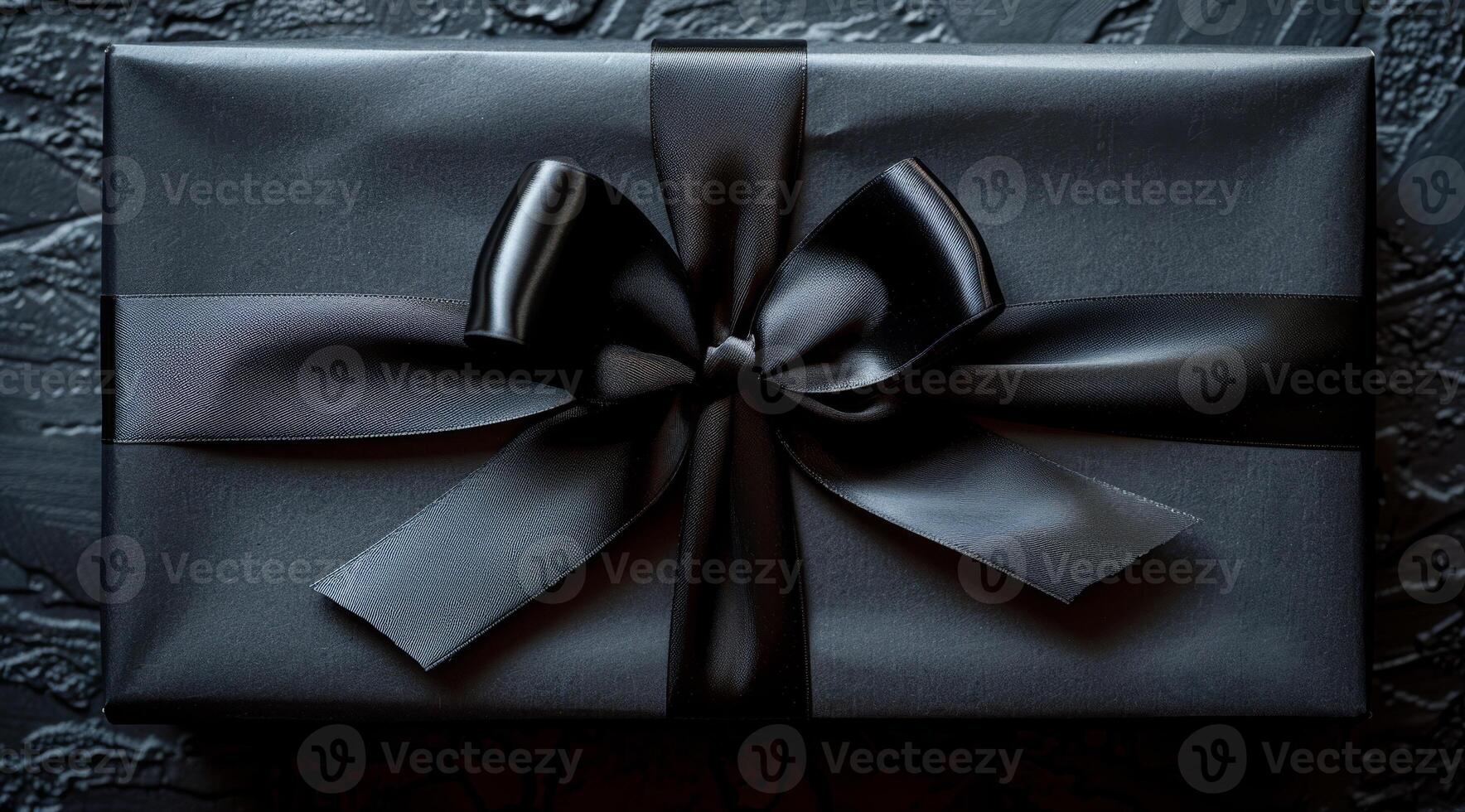A black box with a bow on top of it. The box is wrapped in black paper and has a black ribbon tied around it. The bow is tied in a bow shape and is positioned in the center of the box. photo