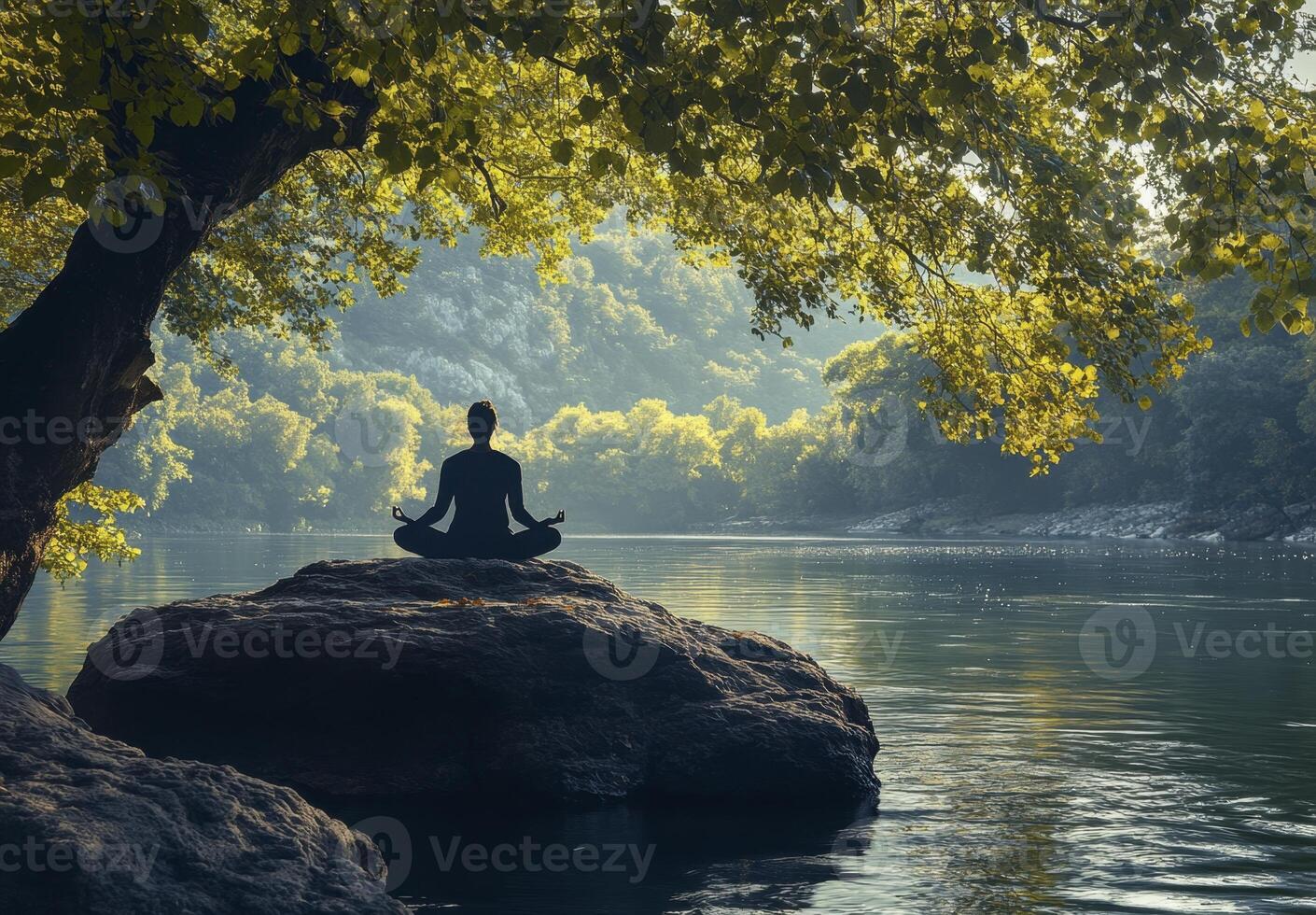 A women finds peace while meditating by the tranquil lake under a large tree. photo