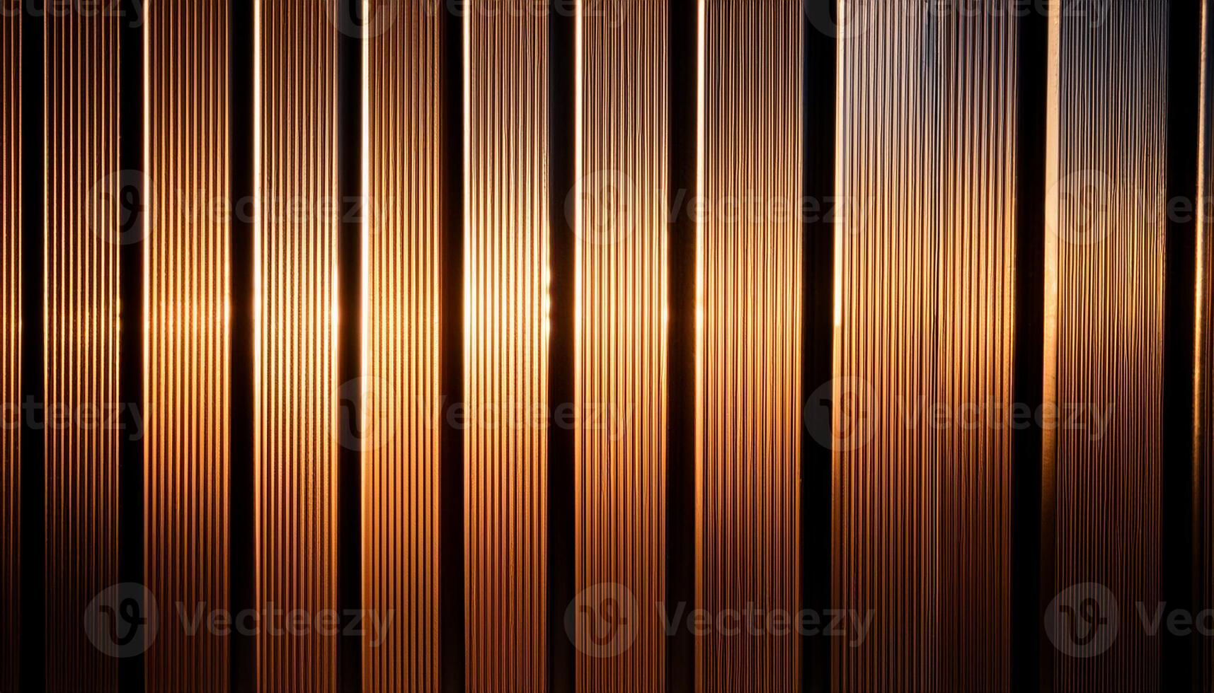 Close-up of vertical metal lines illuminated by warm golden light, creating a modern, industrial, and textured pattern. photo