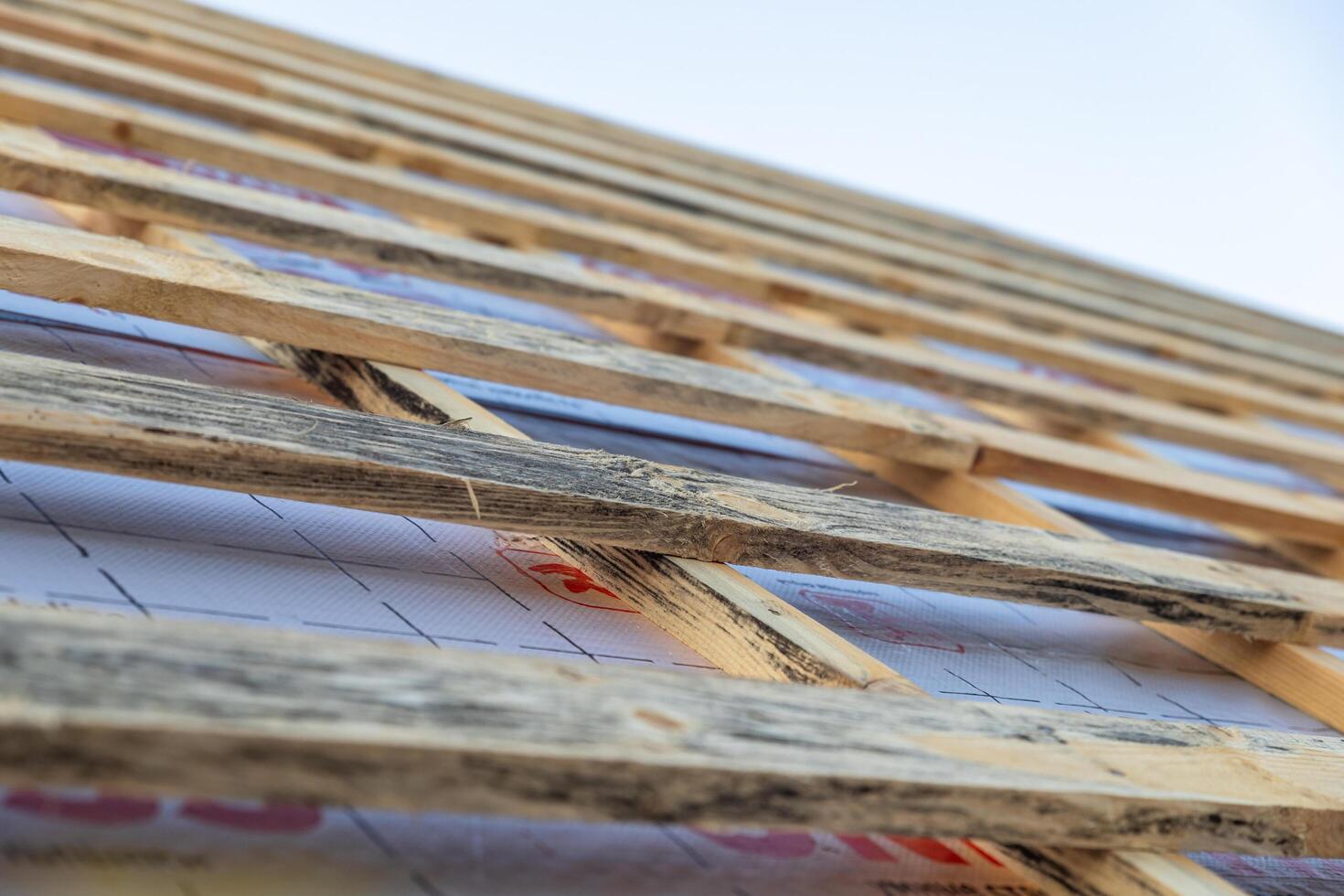 lose-up of a wooden roof frame during construction. The wooden planks are arranged in a grid pattern and supported by beams, creating a sturdy foundation for the roof. photo