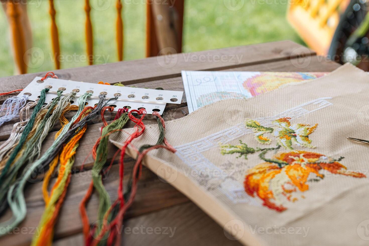 Close-up of a cross-stitch in progress. Cross-stitch with various colorful threads, a needle, and a pair of embroidery scissors. Intricate embroidery details, as well as the sewing process. photo