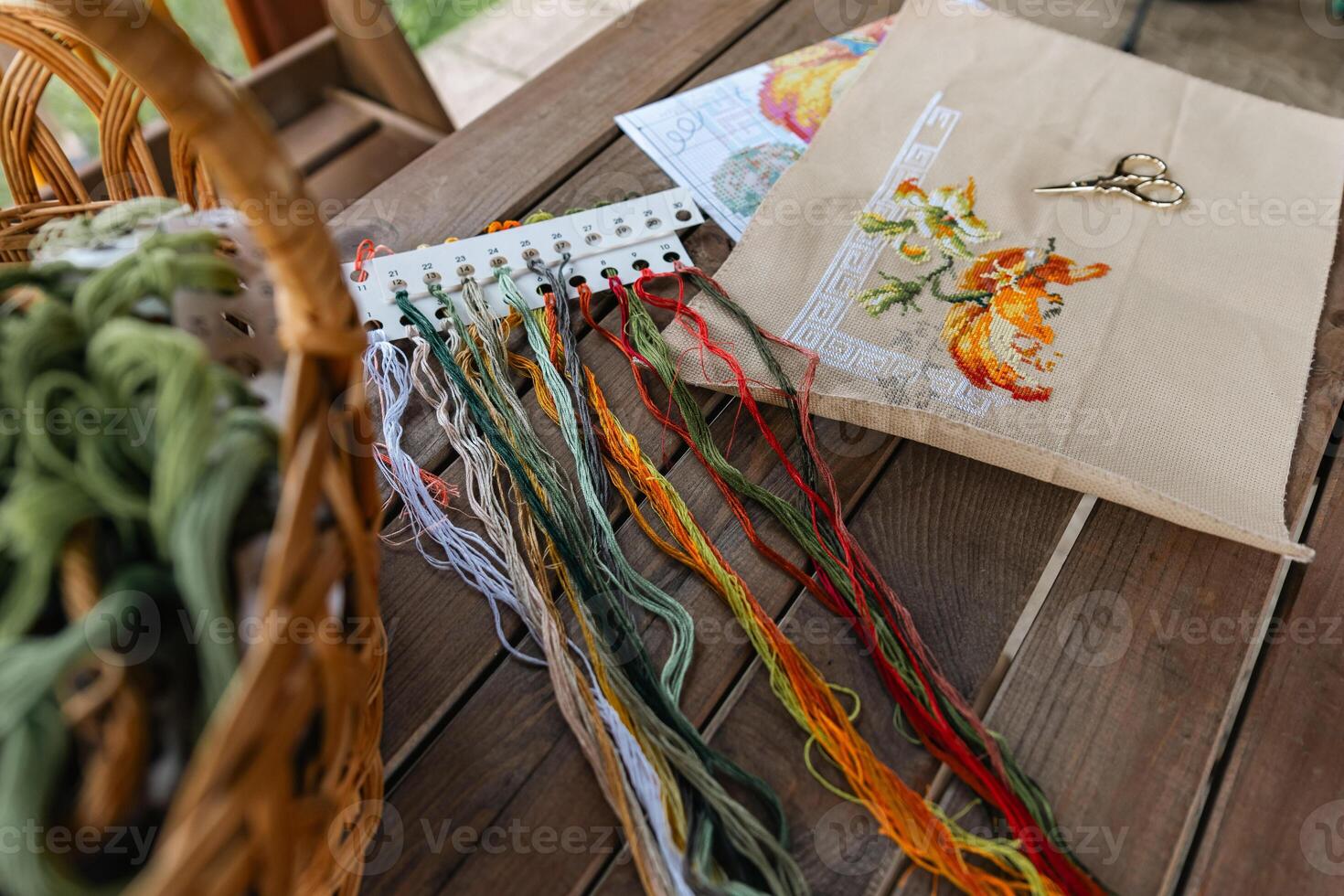 Close-up of a cross-stitch in progress. Cross-stitch with various colorful threads, a needle, and a pair of embroidery scissors. Intricate embroidery details, as well as the sewing process. photo